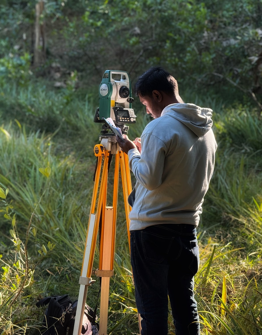 A surveyor beside a total station in tall grass, writing a reading down on paper